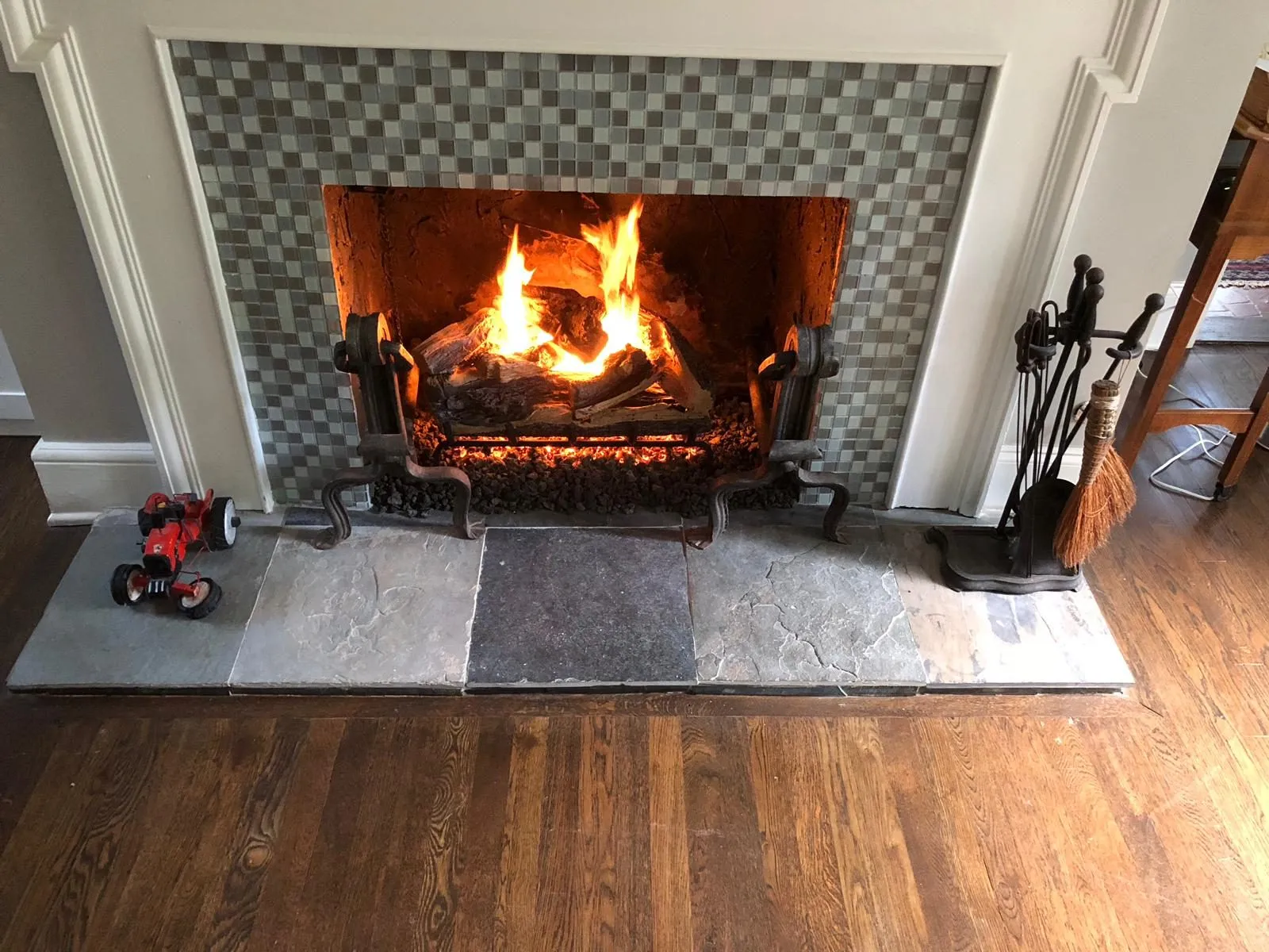 Wide view of a mosaic tile fireplace burning in a living room